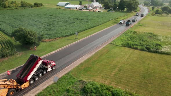 Road crew working on repaving a section of rural highway. Several dump trucks supply asphalt.