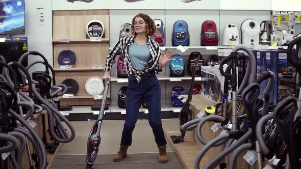 Funny Caucasian Woman in Casual Standing in Home Appliance Store Dancing Having Fun with Hand Helded alt