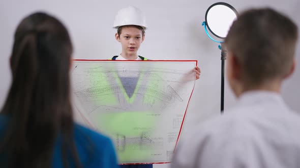 Portrait of Confident Teenage Foreman in Uniform Talking Showing Blueprint alt