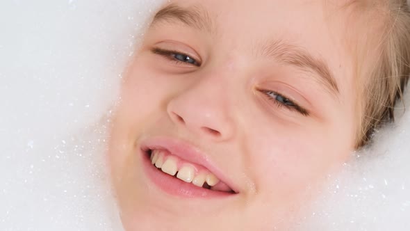 Portrait of Cheerful Teen Girl Lying in Bath with Thick Soap Foam and Looking in Camera alt