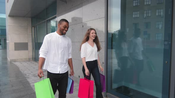 Young Positive Multiethnic Couple Leaving Store Together with Purchases Walking in City Outdoors alt