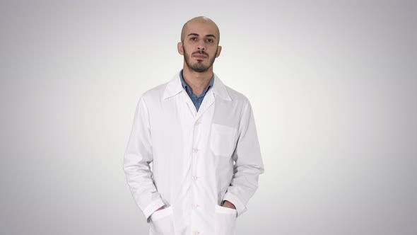 Arab Handsome Doctor Wearing His Uniform Walking with Hands in Pockets on Gradient Background. alt