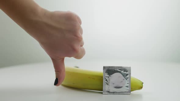 Closeup Contraceptive and Banana at White Background with Female Hand Gesturing Thumb Down alt