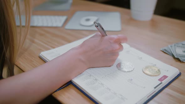 Woman with Bitcoins Writing Into Daily Planner. Crop View of Female with Pen Writing Data in Daily alt