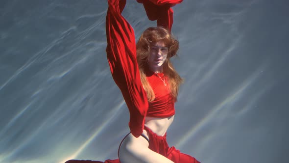 Attractive Redhaired Young Woman Swims Beautifully Underwater in a Red Dress alt