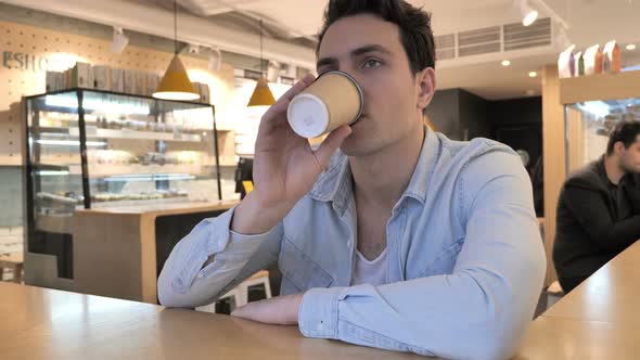 Young Man Drinking Coffee in Cafe alt
