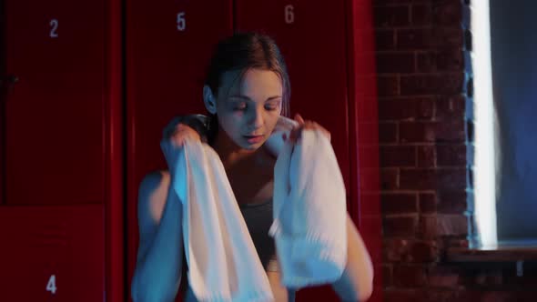 Sports  Young Woman Sitting in Locker Room and Putting a Towel on Her Neck alt