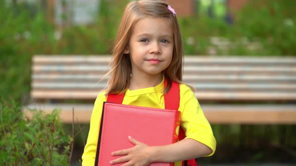 Girl Holds Book in Schoolyard and Smiles