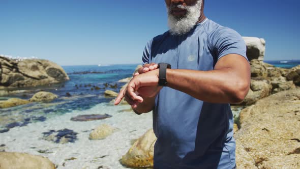 Senior african american man exercising using smartwatch on rocks by the sea alt