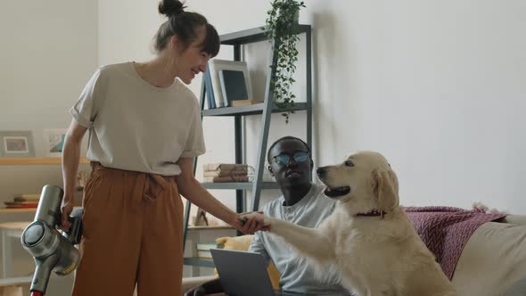 Happy Multiethnic Couple Petting Dog on Sofa at Home alt
