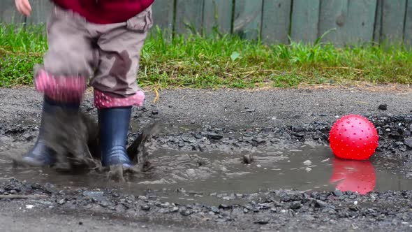 Child in Rubber Boots Jumps in a Puddle and Make Sprays, in the End He Move Out from Shot.