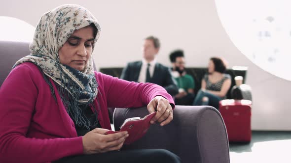 Woman with headscarf waiting in airport departure lounge on mobile phone