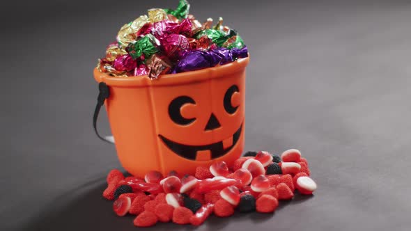 Scary halloween pumpkin printed bucket full of candies against grey background alt