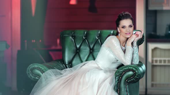 Smiling Luxury Woman Posing in Amazing Glamour White Dress Sitting on Armchair Looking at Camera alt