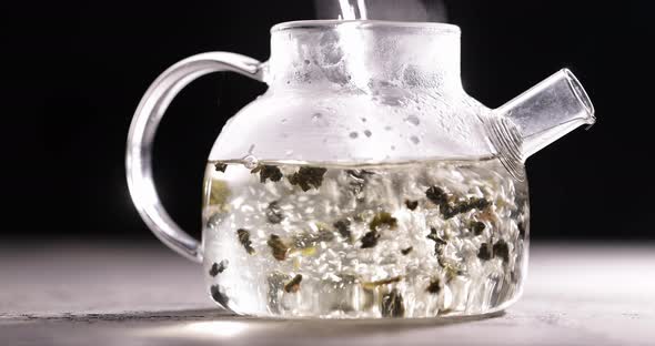 Process of Brewing Herbal Tea in Glass Transparent Teapot at Dark Background alt