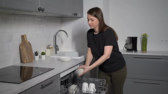 Young Woman in the Kitchen Opens the Dishwasher Loads and Takes Out Dishes