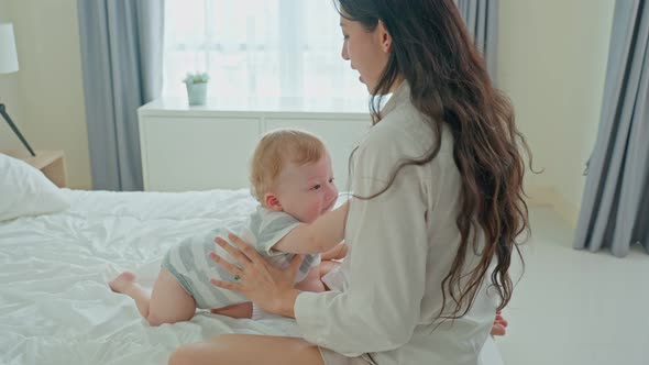 Caucasian loving mom play with cute baby boy child on bed in bedroom in the morning at house. alt