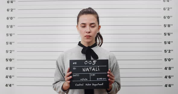 Portrait of Young Woman with Ponytail Holding Sign for Photo in Police Department alt