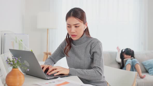 Asian business woman work at home with young kid daughter play around and loss concentration on job alt