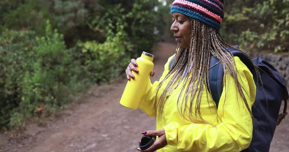 Senior african woman drinking water during trekking day into the wood alt