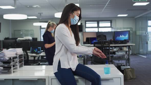 Woman wearing face mask sanitizing her hands at office alt