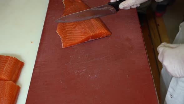 Chef cutting smoked salmon fillets and sliding it off to nearby table - top down view alt