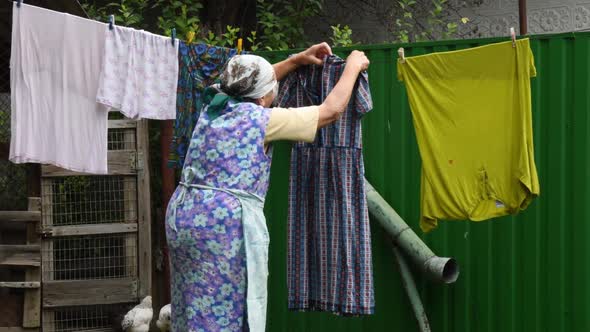 Senior Woman in Traditional Clothes Hang Laundry on Clothespins Outdoor at Rural Backyard with