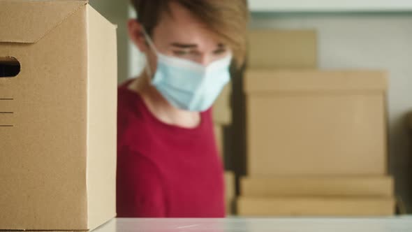 Man Wearing Medical Face Mask and Protective Gloves Putting Parcel on Shelf Employee of Warehouse alt