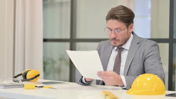 Middle Aged Engineer Reading Reports while Sitting in Office alt