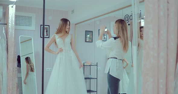 Beautiful Girl Wore an Elegant Wedding Dress and Does a Fitting in Front of a Mirror alt