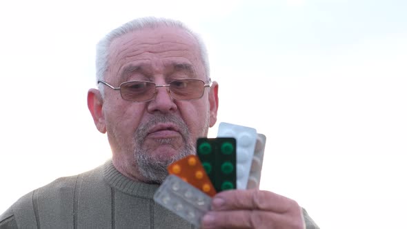 Sick Old Mature Grayhaired Man Grandfather Holding a Pack of Pills in His Hands alt