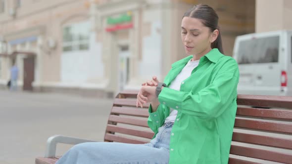 Hispanic Woman Checking Time While Waiting on Bench Outdoor alt