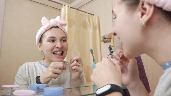 A Cute Girl is Brushing Her Teeth with Dental Floss in the Bathroom in Front of the Mirror Busy with alt