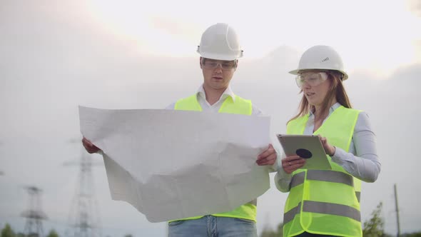 Engineers in Uniform Working with a Laptop Near Transmission Lines alt