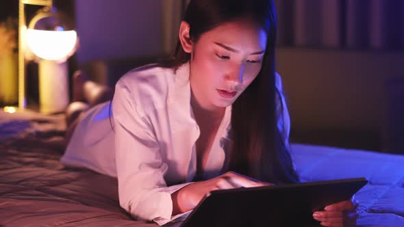 Young Asian beautiful woman enjoy using smartphone in bedroom at night time. alt