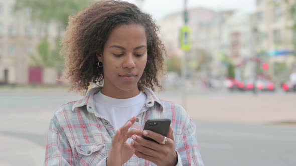 African Woman Browsing Internet on Smartphone Outdoor alt