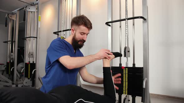 Professional Physical Therapist Lifting Injured Leg of Patient Massaging It alt