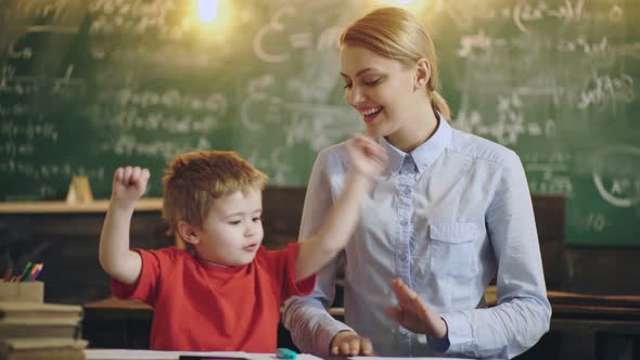 Smiling Teacher Helping a Little Student at the Elementary School alt