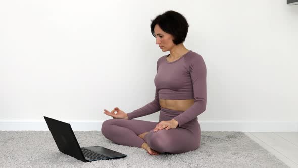 Pretty fitness young woman in violet sportswear practicing yoga exercise in lotus pose