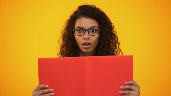 Smart Biracial Female Millennial Shocked With Scientific Facts, Holding Red Book alt