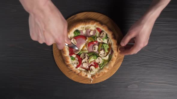 Male Hands Cut Pizza with Pizza Knife on Wooden Background