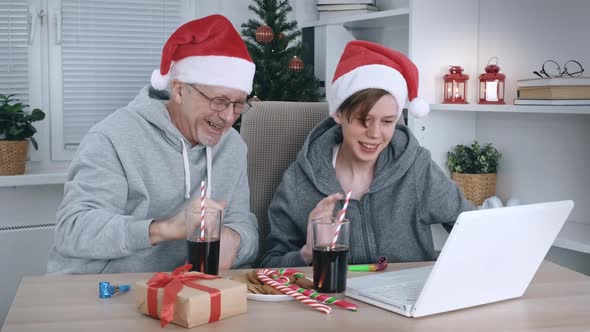 An Elderly Father and a Teenage Son in Santa Hats Communicate Via Video Link with Relatives Using a