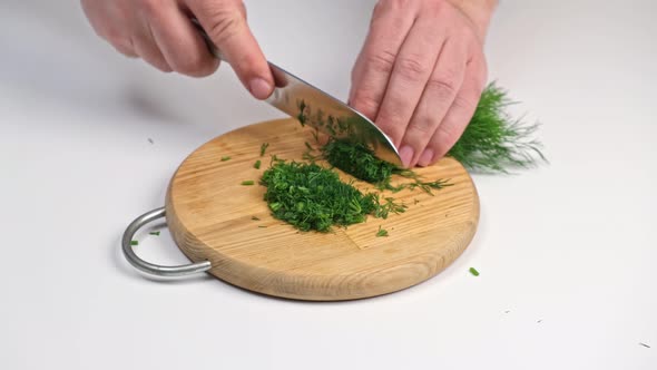 Male hands cut fresh dill on a cutting board close-up with a knife.