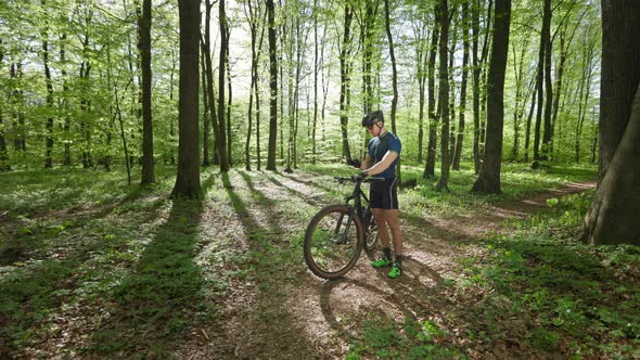 A Cyclist is Standing in the Middle of the Forest and Looking at the Training Data on His Smartphone alt