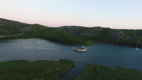 Aerial drone shot of a ferry in the river with sailboats anchored by the shore in Skradin in Šibenik alt