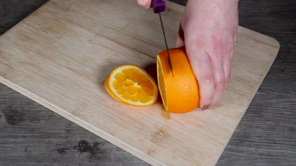 A woman in a kitchen cutting an orange on a wooden chopping board fruit salad alt