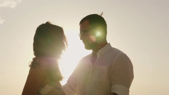 Silhouettes of Man and Woman Kissing Against the Sky in a Hot Sunny Day alt