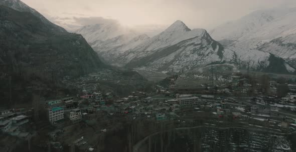 Wide rotating shot of houses build up above the mountain with snow caped mountain in the background. alt