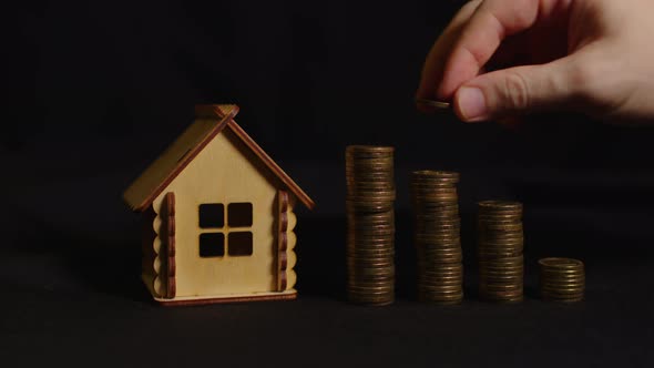Small Wooden House with Columns of Coins on Black Background alt
