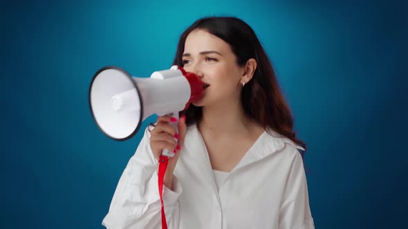 Beautiful Young Woman Shouting Into Loudspeaker Against Blue Background